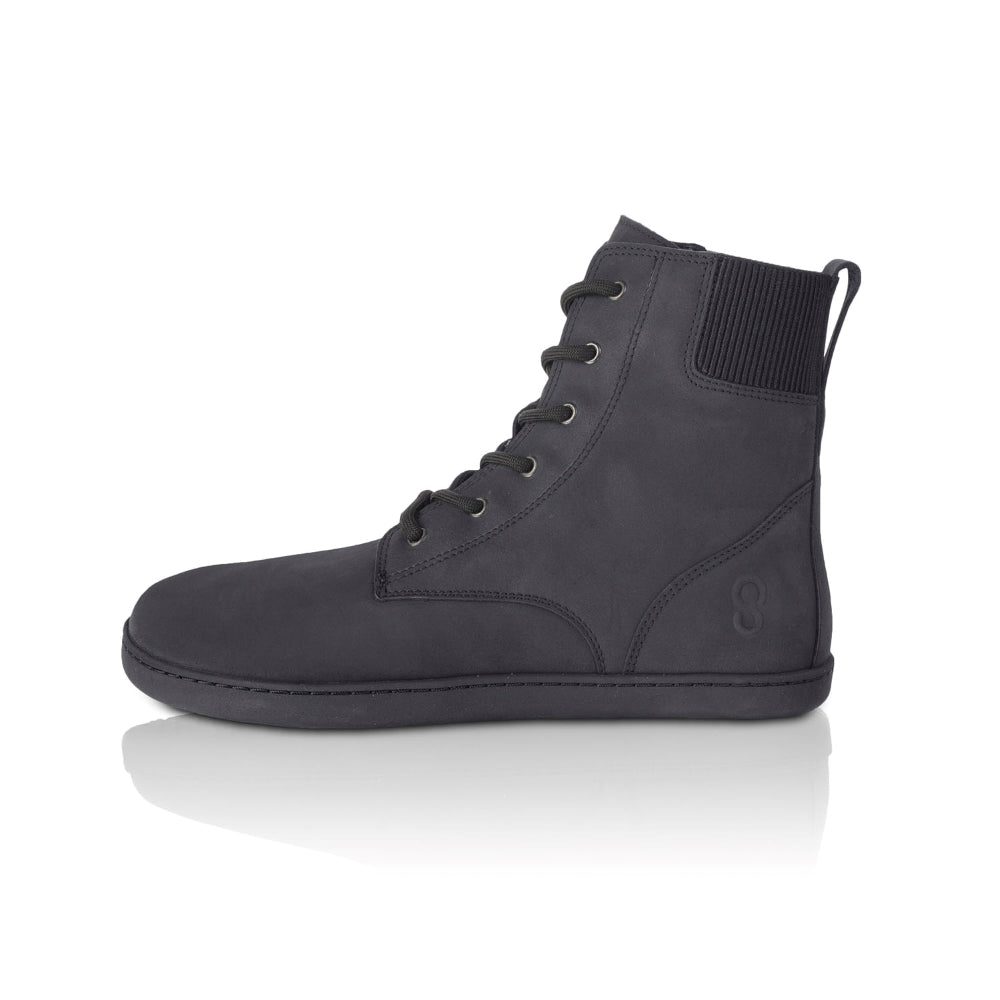 A photo of the Shapen Urbaneer combat boots made with nubuck leather, a thin wool lining, and rubber soles. The boots are black in color and have an elasticized panel on the top back of the boot. The left boot is shown from the left side on a white background. #color_black