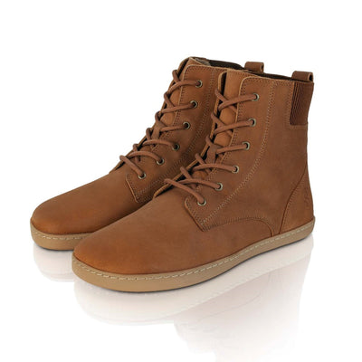 A photo of the Shapen Urbaneer combat boots made with nubuck leather, a thin wool lining, and rubber soles. The boots are caramel brown in color and have an elasticized panel on the top back of the boot. Both boots are shown together diagonally from the front left side on a white background. #color_caramel