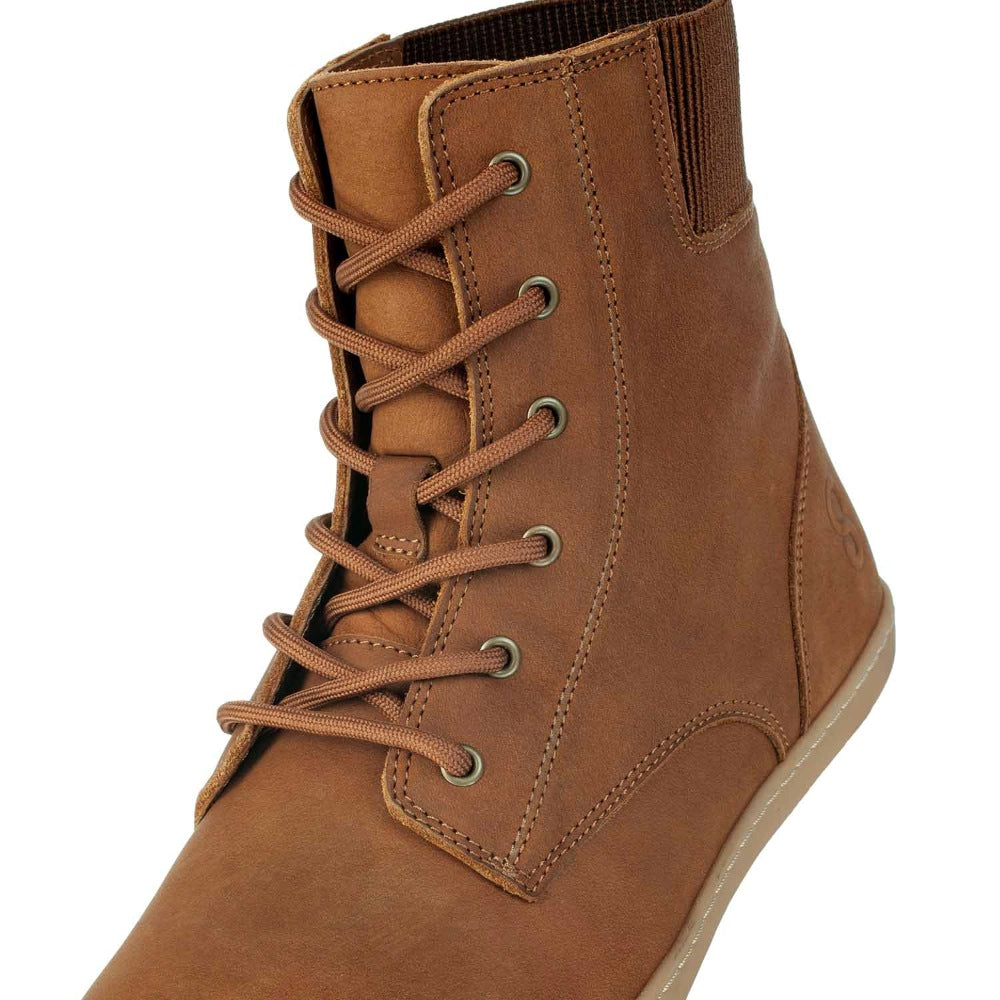 A photo of the Shapen Urbaneer combat boots made with nubuck leather, a thin wool lining, and rubber soles. The boots are caramel brown in color and have an elasticized panel on the top back of the boot. The right  boot is shown from the front zoomed in on the laces, on  white background. #color_caramel
