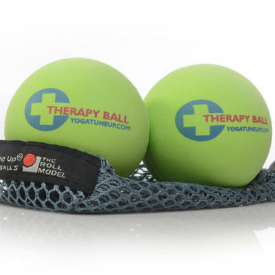 A photo of Tune Up therapy balls made from rubber. The therapy balls are a light green color with therapy ball written on one side and yoga tune up on the other. Both balls are shown sitting on a gray mesh bag against a white background. 