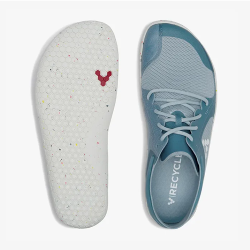 A photo of Vivobarefoot Primus lite sneakers made from recycled plastic and a rubber sole. The athletic sneakers are a blue haze color with white soles spotted with color with the vivobarefoot logo on the side. Both shoes are shown beside each other, the right shoe is facing upright and seen from the top and the left shoe is shown upside down to show the sole against a white background. #color_blue-haze
