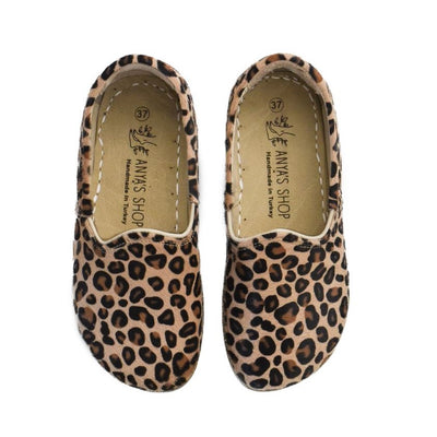 A photo of Yasemin Leather loafers Designed by Anya with a leather upper and tan rubber soles. The loafers are a leopard print color with a calf hair leather upper and have a small curve up on the top of the foot for design. Both loafers are shown from the top facing down against a white background. #color_leopard-print-calf-hair