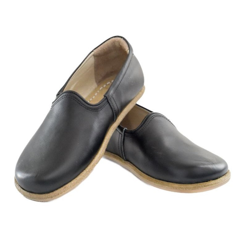 A photo of Yasemin Leather loafers Designed by Anya with a leather upper and tan rubber soles. The loafers are a black color with a smooth leather upper and have a small curve up on the top of the foot for design. Both loafers are shown facing opposite directions with the heel of the right shoe is leaning on the left shoe against a white background. #color_black-smooth-leather