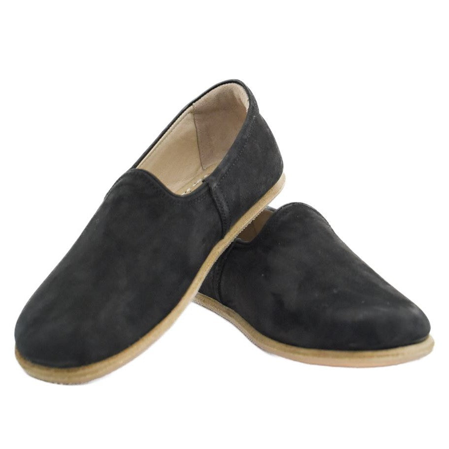 A photo of Yasemin Leather loafers Designed by Anya with a leather upper and tan rubber soles. The loafers are a black color with a nubuck leather upper and have a small curve up on the top of the foot for design. Both loafers are shown facing opposite directions with the heel of the right shoe is leaning on the left shoe against a white background. #color_black-nubuck