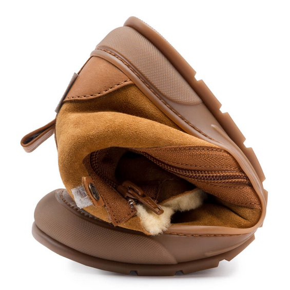 A photo of Zapatos Feroz Alcoy made with suede, sheepskin, and rubber soles. The boots are nut brown in color with rubber around the soles and a zipper on the side. One boot is shown rolled into a ball to show flexibility against a white background. #color_nut-brown
