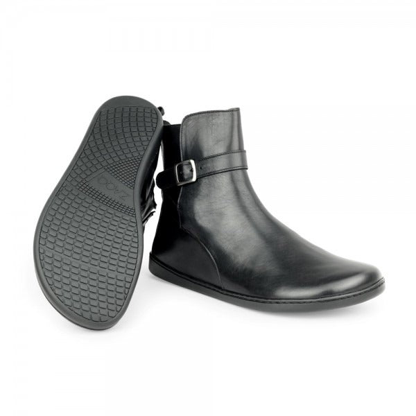 A photo of Zaqq Riquet boots made from Nappa leather and rubber soles. The boots are black in color and a pull up style with a decorative buckle around the ankle. Both boots are shown one boot is shown from the right side and the other is laying upside down to show the sole against a white background.  #color_black