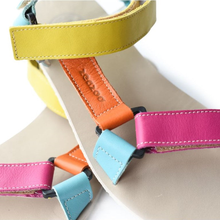 A photo of Zeezoo Olymp Rainbow sandals made from leather with velcro and a light beige leather topped rubber soles. The sandal straps are pink, light blue, orange, and yellow. The straps cross the front of the foot and a single strap runs along the outside of the top of the foot and around the ankle and heel. Both sandals are on top of each other and the left sandal is shown up close from above against a white background. #color_rainbow-olymp