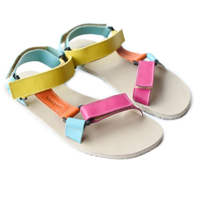 A photo of Zeezoo Olymp Rainbow sandals made from leather with velcro and a light beige leather topped rubber soles. The sandal straps are pink, light blue, orange, and yellow. The straps cross the front of the foot and a single strap runs along the outside of the top of the foot and around the ankle and heel. Both sandals are shown beside each other from above and turned slightly to the right side against a white background. #color_rainbow-olymp