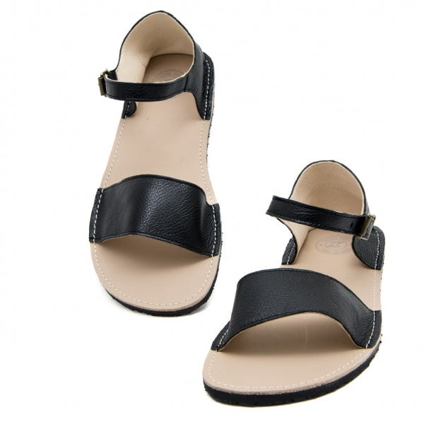 A photo of Zeezoo Siren Black Sandals made of leather and a light beige leather topped black rubber sole. The sandals have a front foot crossing strap, a leather ankle strap and heel cup. Both sandals are shown from the front with the left sandal leaned upright against a white background. #color_black